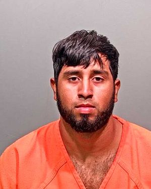 A man with dark hair and a beard is shown facing the camera while wearing an orange prison uniform.