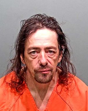 A middle-aged man with long hair and a goatee is shown wearing an orange prison jumpsuit in a mugshot.
