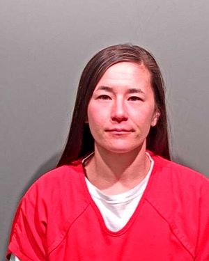 A woman with long dark hair is wearing an orange prison jumpsuit and looking at the camera.