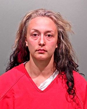A woman with mixed-length hair wearing a red jumpsuit is shown in a mugshot.