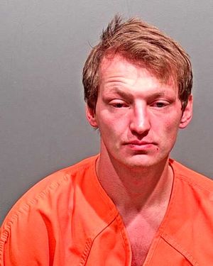 A man wearing an orange jail jumpsuit is shown in a mugshot against a gray background.