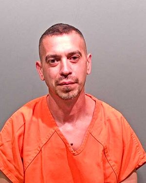 A man wearing an orange jumpsuit poses for a mugshot against a plain background.