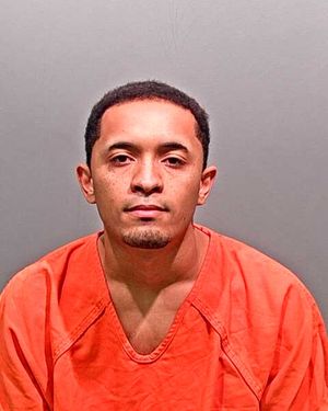 A young man is shown in a mugshot wearing an orange prison jumpsuit against a gray background.