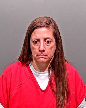 A woman in a red prison outfit is seen against a gray background, looking serious and somber.