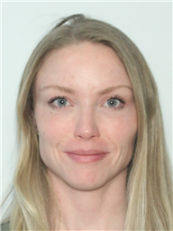 A woman with long, light hair and blue eyes is looking directly at the camera against a plain background.