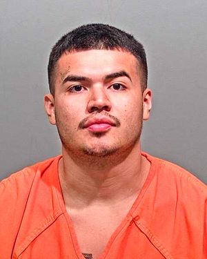 A young man with short hair and a mustache is shown in a mugshot wearing an orange prison jumpsuit.