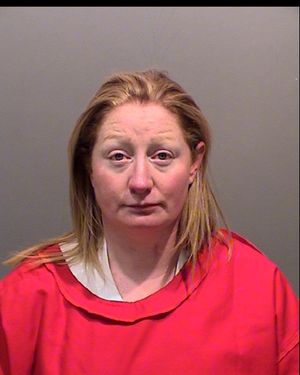 A woman with long, straight hair is wearing a red prison jumpsuit and looking directly at the camera.