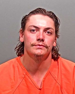 A man with a distinctive mustache is wearing an orange prison jumpsuit and looking directly at the camera.