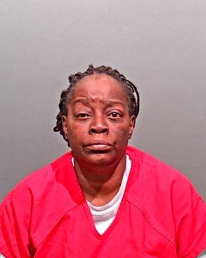 A woman with braided hair is shown wearing a red prison jumpsuit, looking directly at the camera.