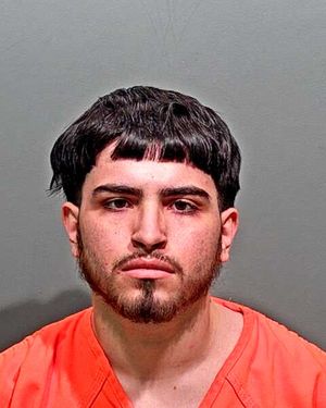 The image shows a young man with a distinctive hairstyle and facial hair wearing an orange prison jumpsuit.