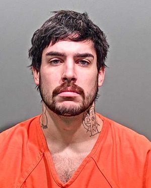 A male wearing an orange jail uniform poses for a mugshot, displaying tattoos on his neck and a serious expression.