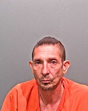 A man wearing an orange jumpsuit poses for a mugshot against a gray background.
