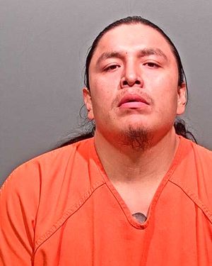 A man with long hair is shown in a prison uniform, looking directly at the camera.