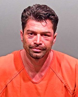 A man with short dark hair, wearing an orange prison jumpsuit, appears in a mugshot with visible bruises on his face.