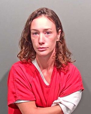 A woman with curly hair, wearing a red prison outfit, is looking directly at the camera.