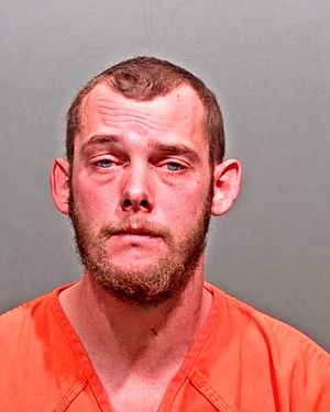 A man wearing an orange jumpsuit is shown in a mugshot with a serious expression and a beard.