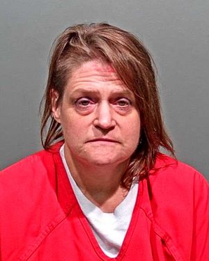 A woman with disheveled hair and a distressed expression is wearing a red prison jumpsuit against a gray background.