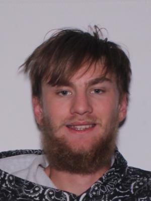 A young man with a beard and messy hair smiles at the camera while wearing a patterned hoodie.