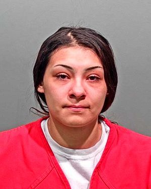 A woman with dark hair is shown in a mugshot wearing a red prison jumpsuit.