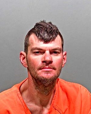 A man with a mohawk and beard is shown in an orange inmate jumpsuit against a plain background.