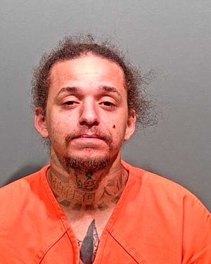 A man with tattoos is shown wearing an orange jumpsuit and looking directly at the camera.