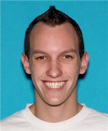 A smiling young man with short, spiked hair poses against a bright blue background.