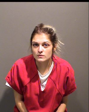 A woman wearing a red prison jumpsuit sits against a neutral background, looking directly at the camera.