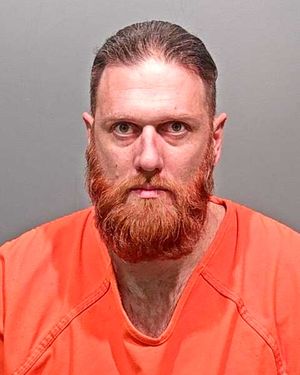 A man with a full red beard wearing an orange prison jumpsuit.