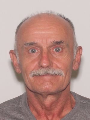 A senior man with a prominent mustache and gray hair is smiling at the camera.