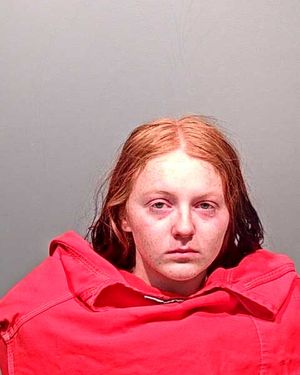 A young woman with reddish hair is shown in a close-up mugshot, wearing a red garment and looking directly at the camera.