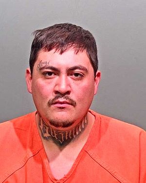 A man with facial tattoos and a neck tattoo is wearing an orange prison jumpsuit.