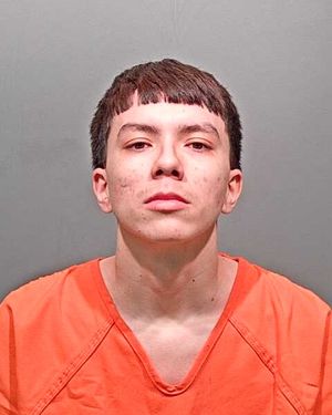 A young man wearing an orange inmate jumpsuit poses for a mugshot against a gray background.