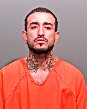 A man with tattoos on his neck is wearing an orange prison jumpsuit and posing for a mugshot.