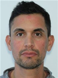 A close-up portrait of a man with short dark hair and a neutral expression against a plain background.