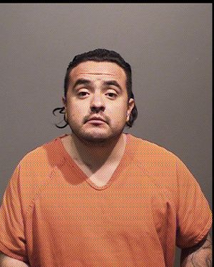 A man wearing an orange prison uniform poses for a mugshot against a neutral background.