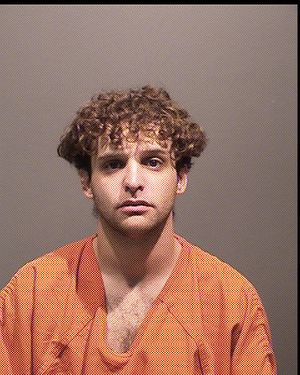 A person with curly hair is shown in an orange jumpsuit, looking directly at the camera against a plain background.
