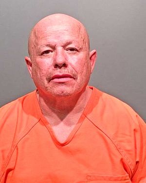 A bald man in an orange prison jumpsuit is facing the camera.