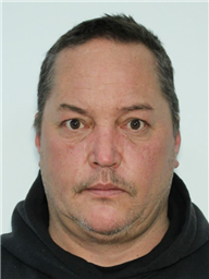 A middle-aged man with short gray hair and facial hair, wearing a dark hoodie, appears to be posing for a photograph.