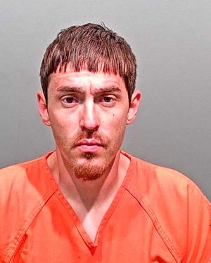 A man with short hair and a goatee is wearing an orange prison uniform and looks directly at the camera.