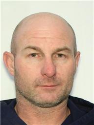 A headshot of a clean-shaven man with short hair, wearing a dark hooded sweatshirt.