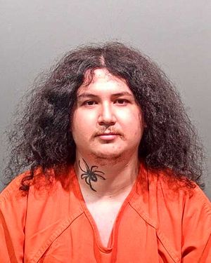 A person with long, curly hair and a spider tattoo on their neck is wearing an orange prison uniform.