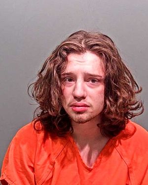 A young man with long curly hair is shown in a mugshot wearing an orange jumpsuit.