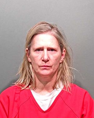 A middle-aged woman with disheveled hair is shown in a mugshot wearing a red prison uniform.