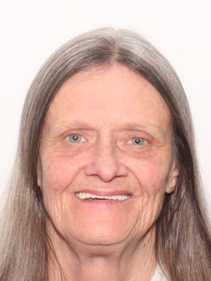 A middle-aged woman with long, straight gray hair and a friendly smile.