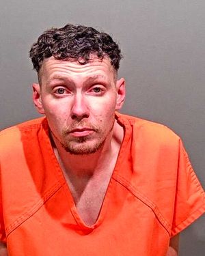 A man wearing an orange prison jumpsuit poses for a mugshot against a plain background.