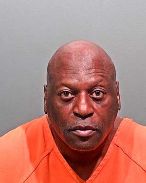 A man in an orange prison jumpsuit stares directly at the camera.