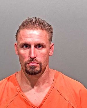 A man wearing an orange prison jumpsuit appears in a mugshot against a plain gray background.