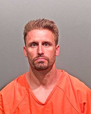 A man with short hair and a beard is wearing an orange jumpsuit and facially expressing concern or sadness.