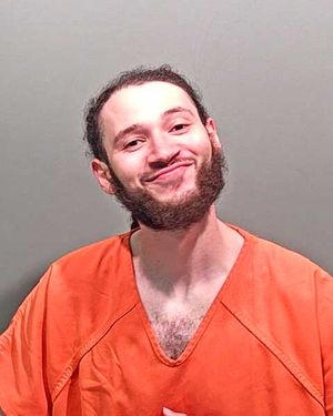 A man wearing an orange prison jumpsuit is smiling at the camera.
