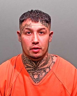 A man with numerous tattoos is wearing an orange jumpsuit and posing for a mugshot.